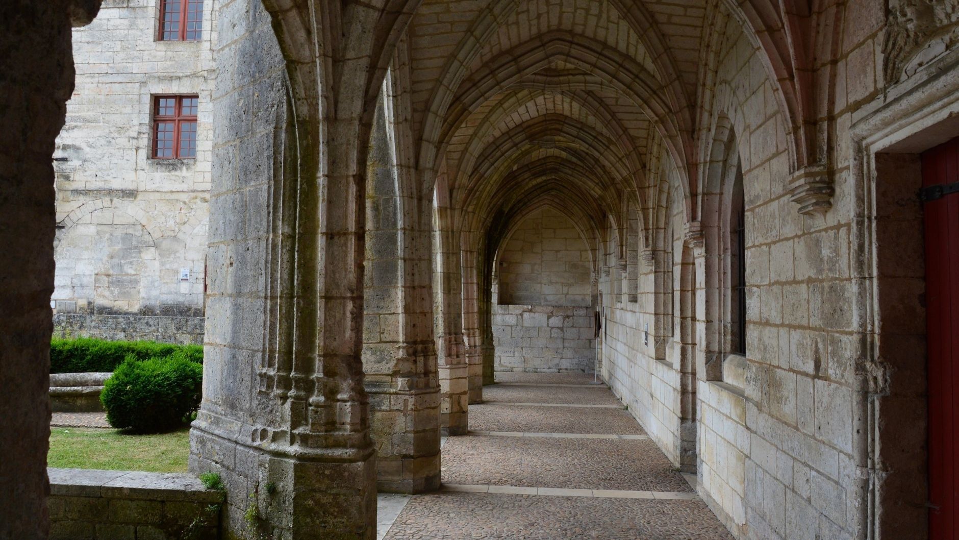 Stone monastery cloister with repeating arches and a garden