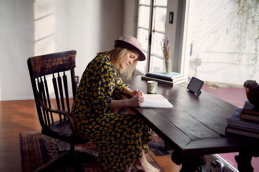 Writer in a floral dress composing notes at a sunlit table