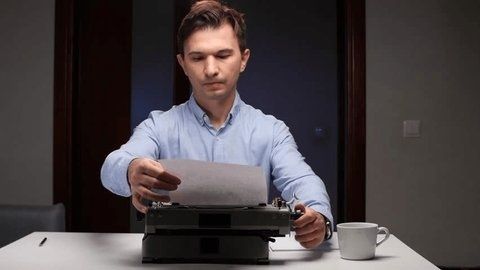Man reviews a sheet of paper beside a vintage typewriter and coffee